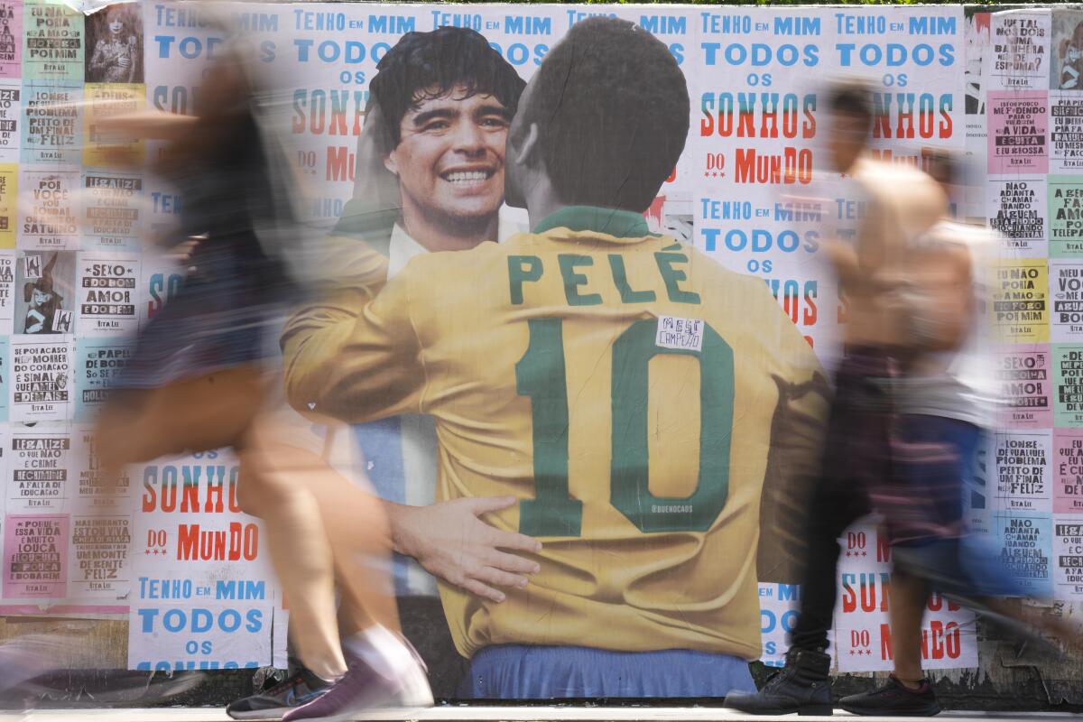People walks past a mural depicting Brazilian soccer legend Pelé embracing late Argentinean soccer star Diego Maradona.