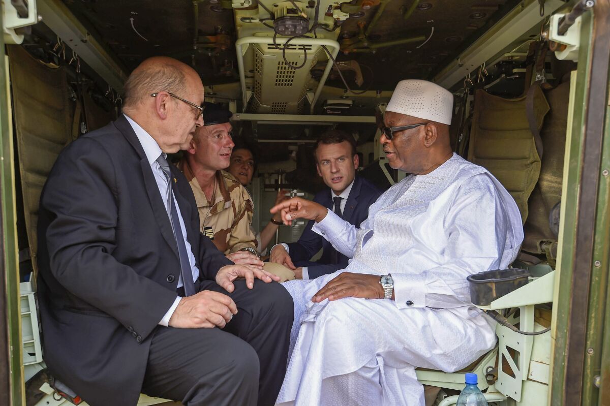 FILE — Mali's former President Ibrahim Boubacar Keita, right, speaks to French Foreign Affairs Minister Jean-Yves Le Drian, left, as French President Emmanuel Macron looks on, during their visit to soldiers of Operation Barkhane in Gao, Northern Mali, May 19, 2017. Paris remained unusually quiet after Mali’s ruling junta this week ordered the French ambassador to leave the West African country. France appears to be seeking to avoid a direct, bilateral confrontation with its former colony, as Bamako's move is only the latest episode in a diplomatic crisis that has gone on for months with African neighbors and European partners. (Christophe Petit Tesson, Pool via AP, File )