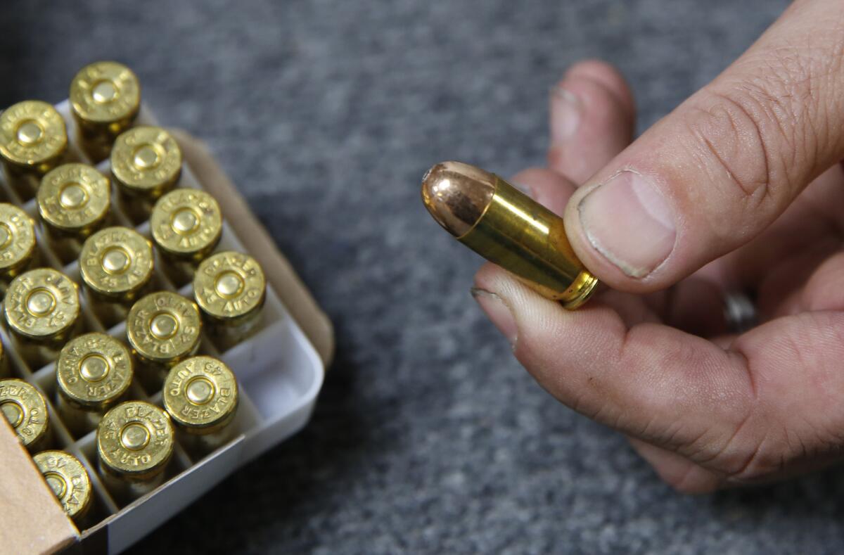 Close-up of .45-caliber rounds in a tray, one held up by fingers