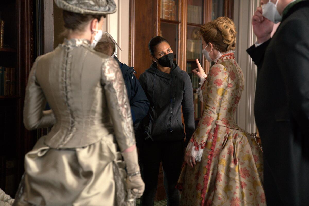 A female director in modern garb talks with two women in period dress on a TV set.