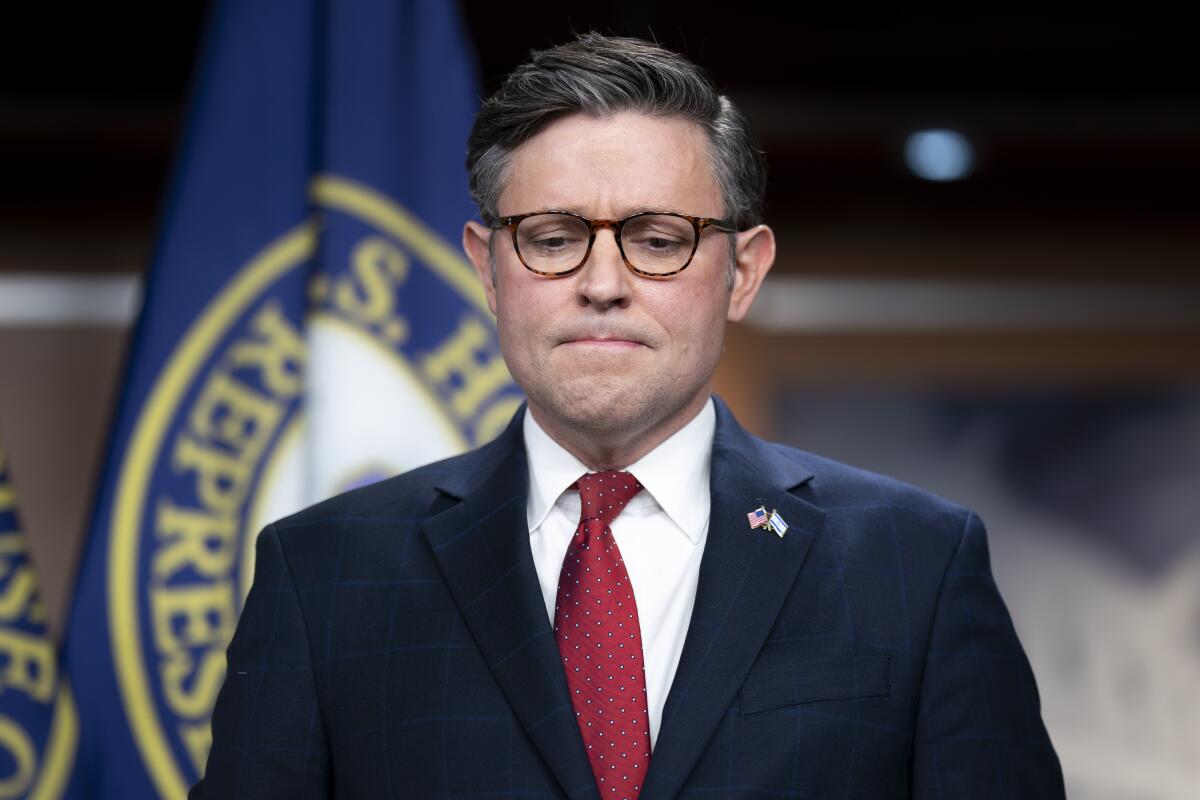 A frowning man in front of the House of Represenatatvies flag 