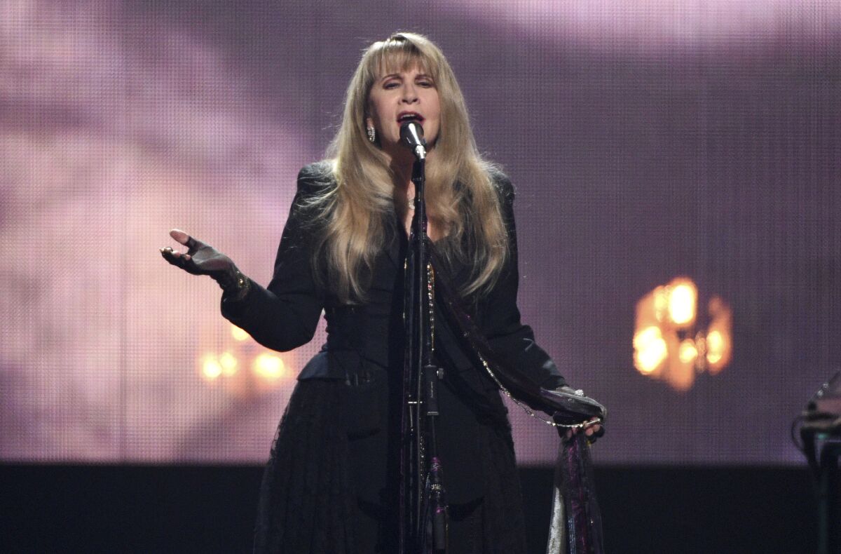 A woman with long, blond hair wearing a black dress and singing into a microphone