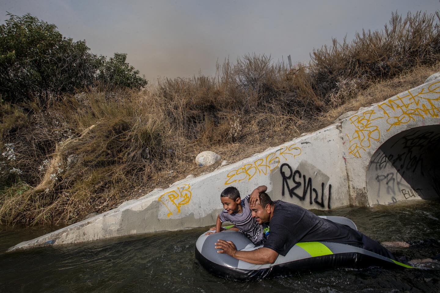 A man and a boy float on an inflatable raft in the San Gabriel River.