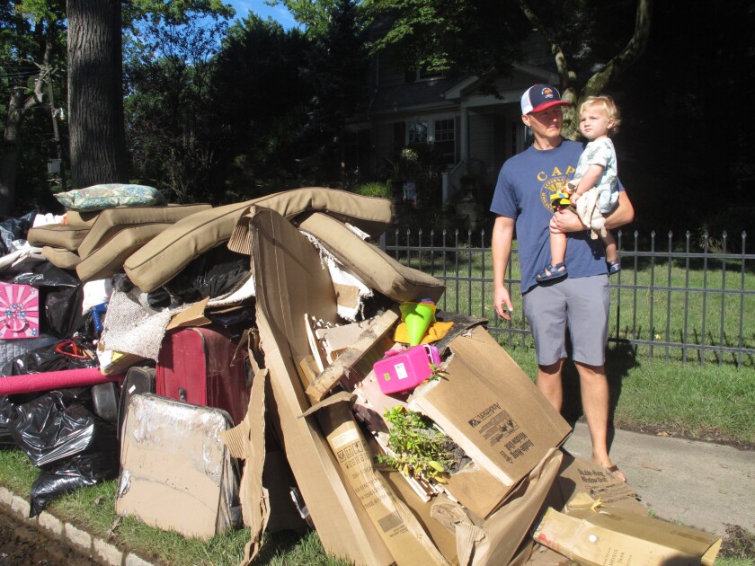 Dave Coughlin carries his infant son Thomas as they are on a sidewalk next to a mound of household items and cardboard boxes