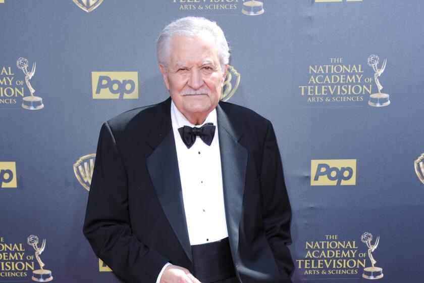An older man in a tuxedo stands on a red carpet