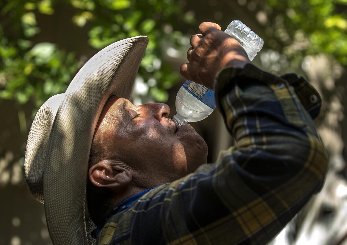A head-and-shoulders profile frame of a man in a plaid shirt and wearing a hat lifting his face upward as he drinks water