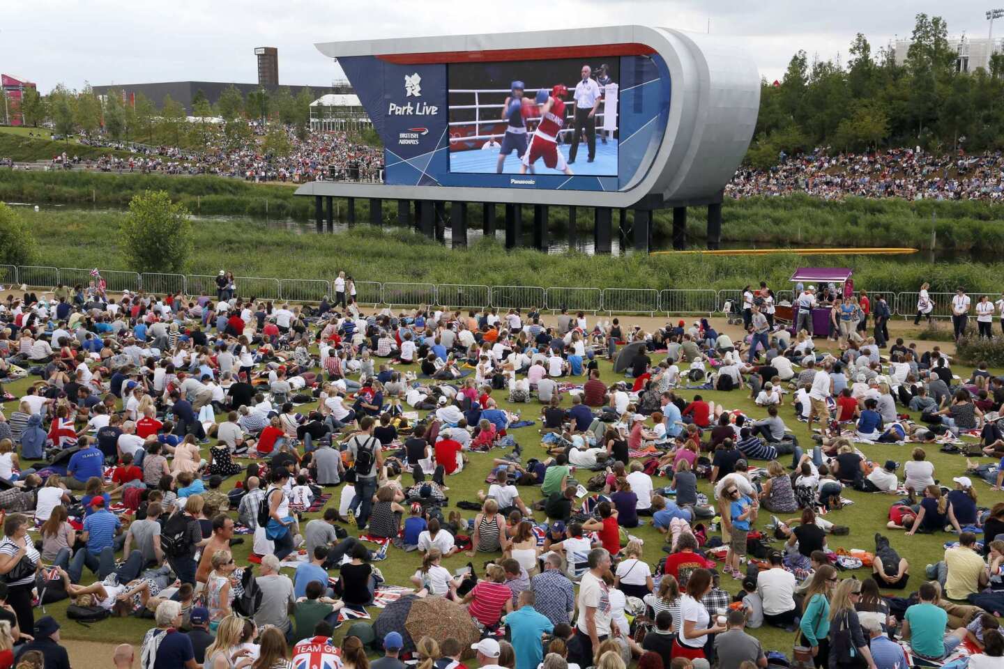Spectators sit on the grass and watch women's boxing on a giant monitor in Park Live, a free area inside Olympic Park.
