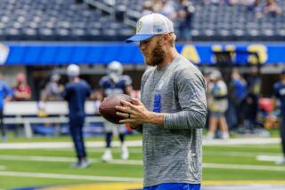 Out of uniform, Cooper Kupp (10) holds a football on the sideline.