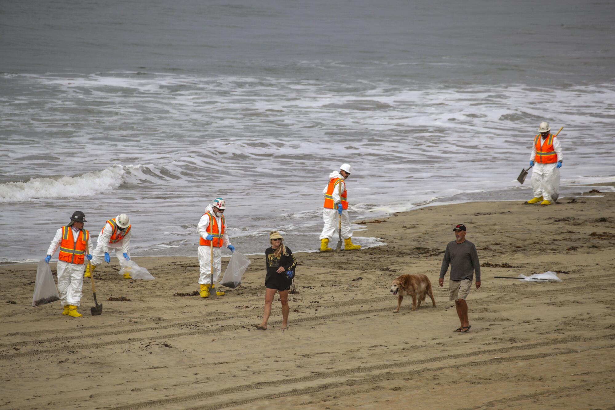 Workers in protective gear comb the beach for oil.