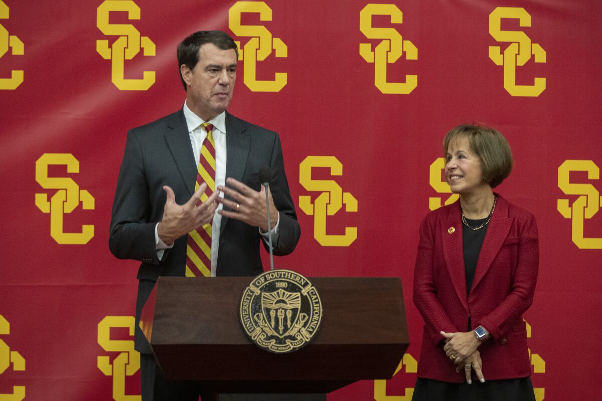 Mike Bohn stands at podium and speaks to a crowd while Carol Folt looks at him and smiles.