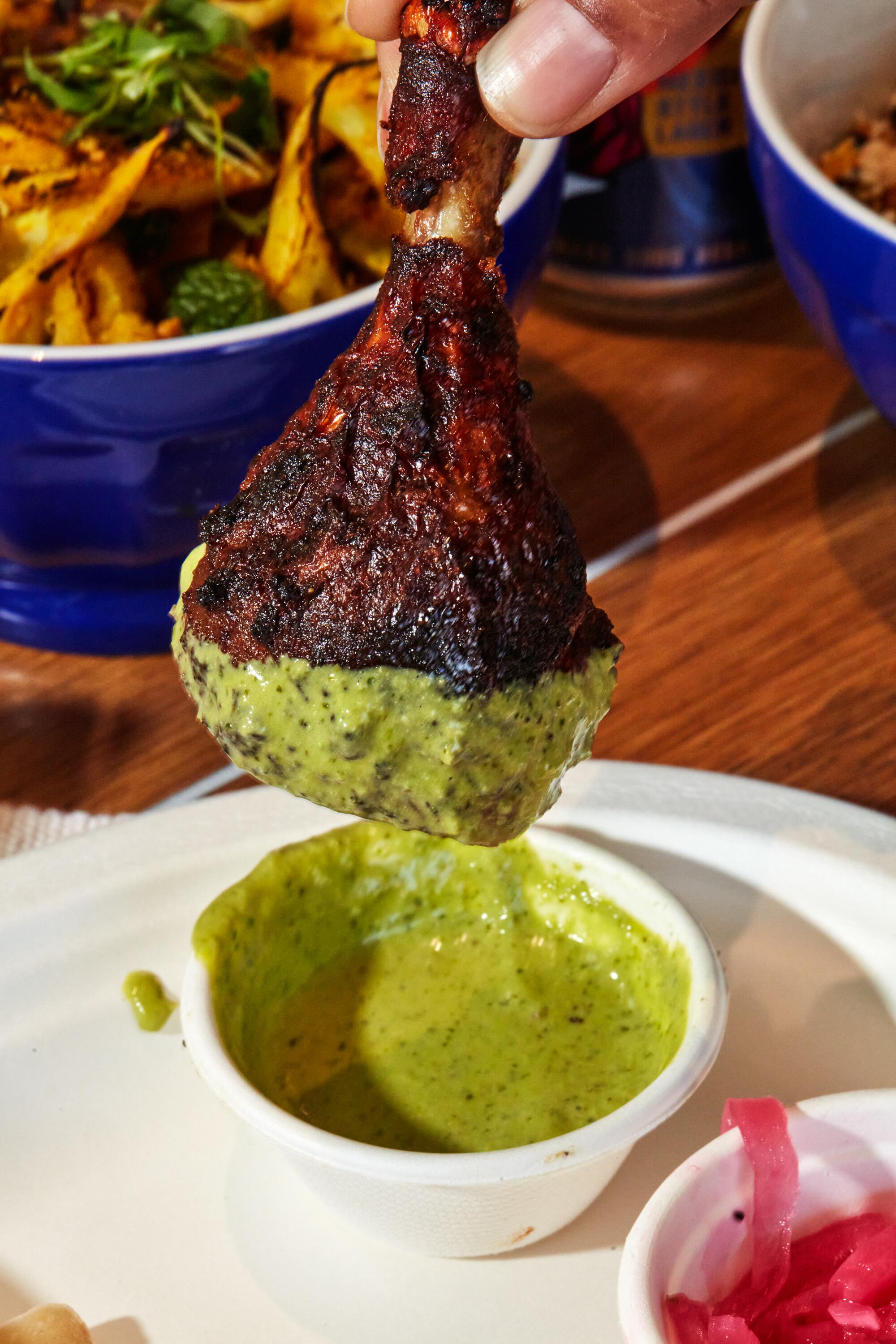 A jeera rotisserie chicken drumstick being dipped into house-made GG sauce