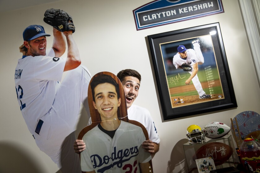 A man, standing against a wall adorned with pictures of Clayton Kershaw, holds an oversize image of himself.