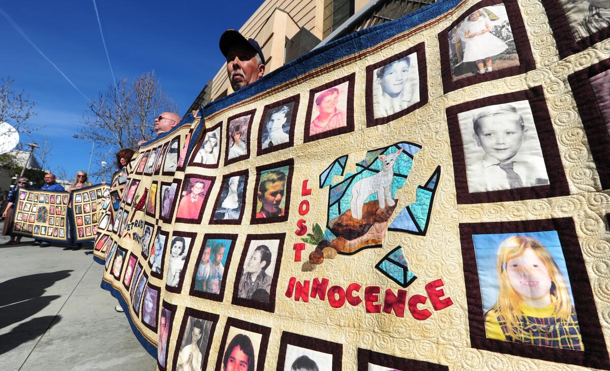 Protesters hold quilts bearing portraits of young children outside the Cathedral of Our Lady of the Angels.