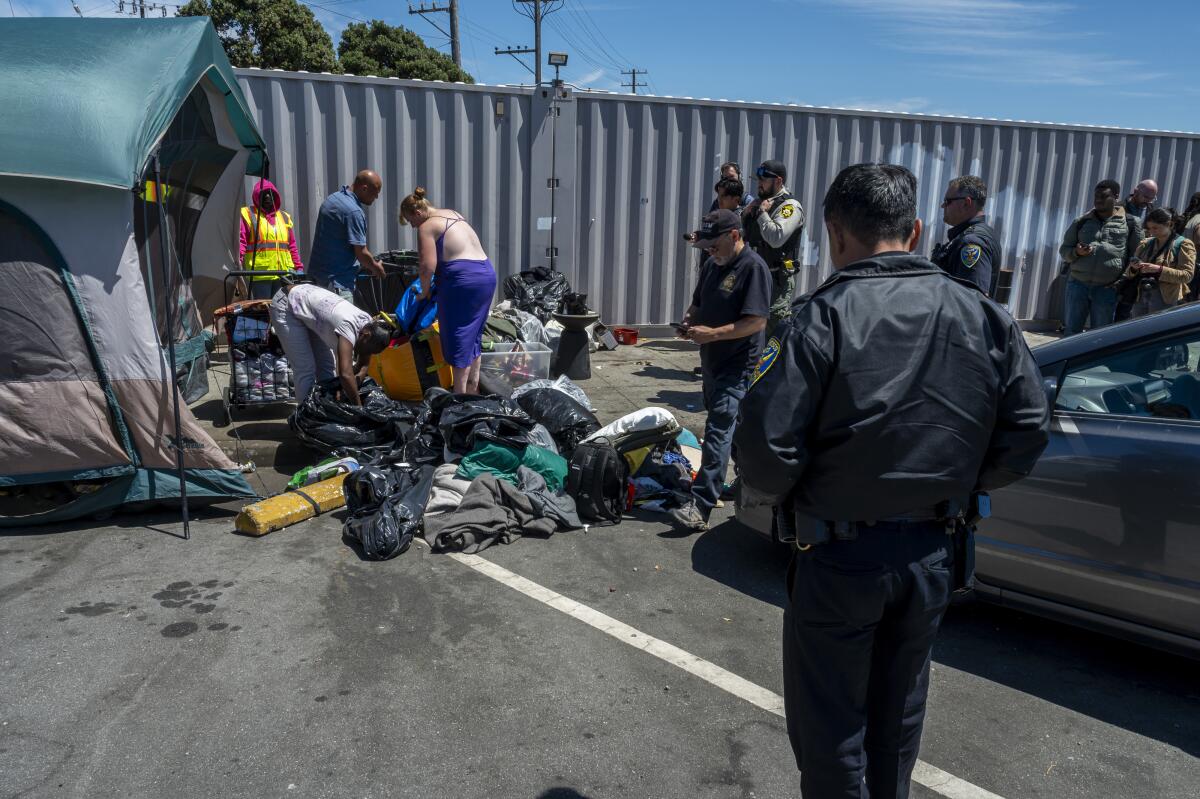 Homeless people collect personal items as workers remove an encampment