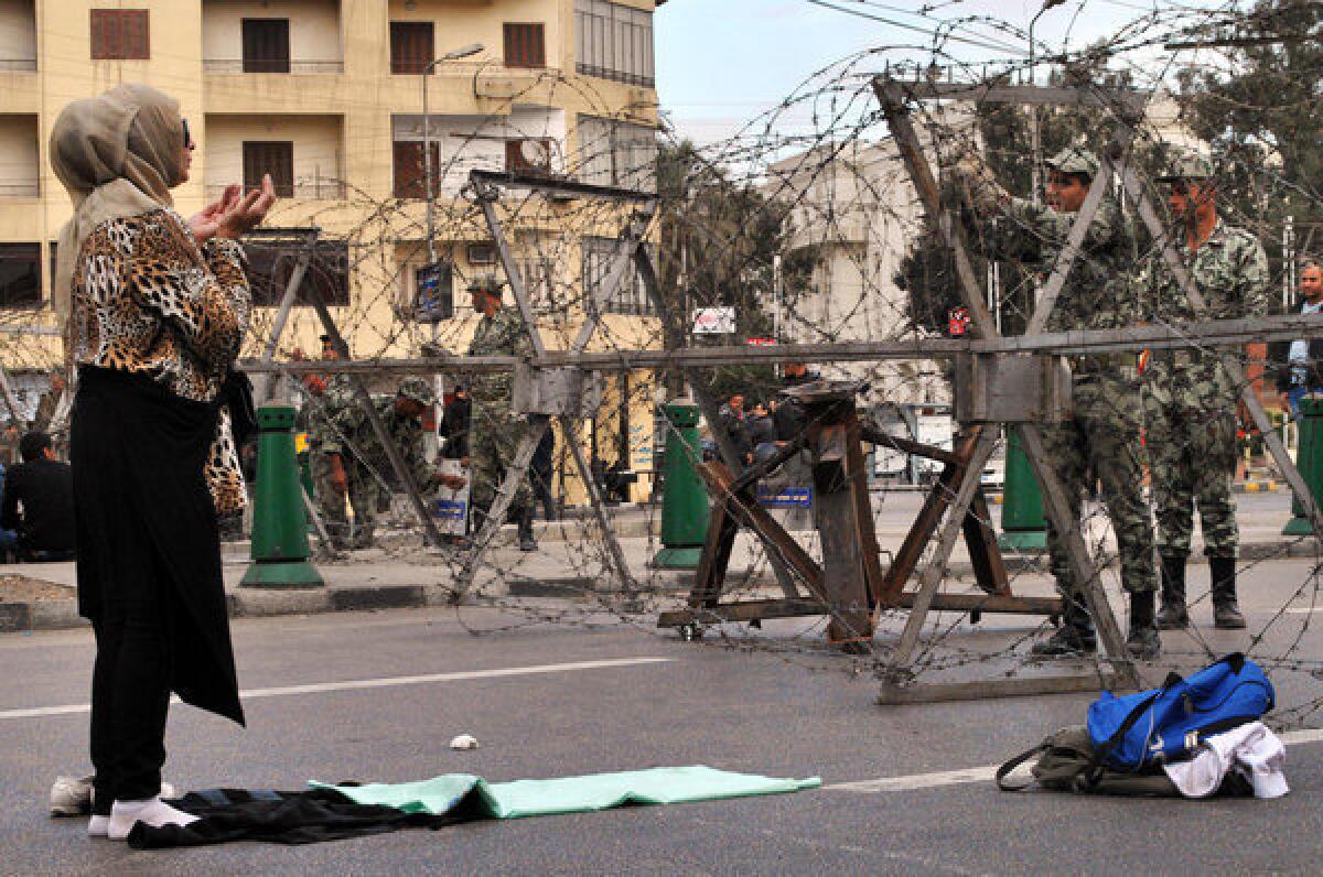 A Egyptian woman prays in front of security forces as they lay out barbed wire along streets leading to the Itihadiya presidential palace in the Heliopolis neighborhood of Cairo ahead of protests on Tuesday.
