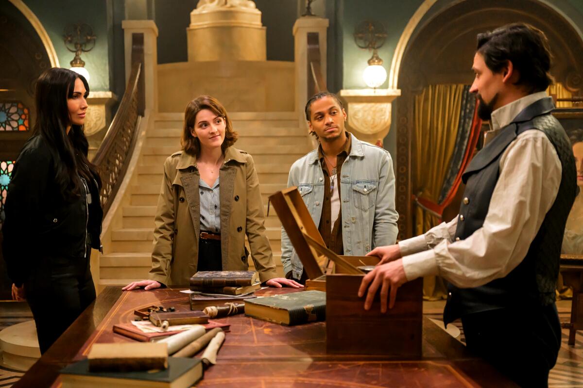 Four characters from "The Librarians: The Next Chapter" stand around a table