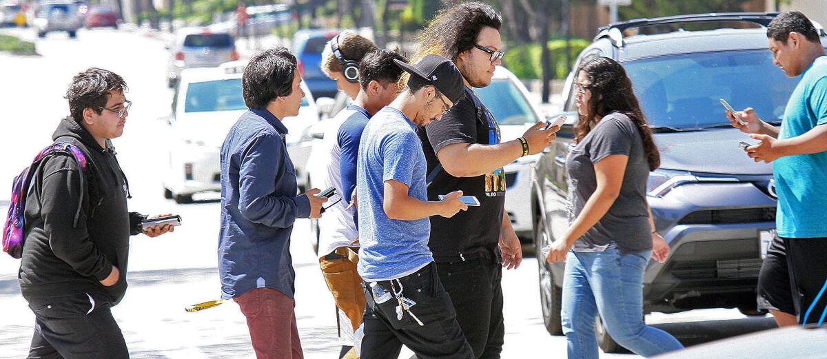 Pedestrians, many of them playing the game Pokemon Go on their smartphones, walk across North 3rd Street in Burbank on Friday. The gamers are looking for local icons to gain experience points for the game.
