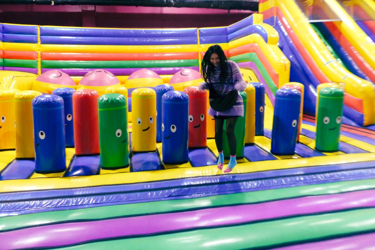 A woman jumps on an inflatable bounce castle; parts of the bounce house have faces printed on them.