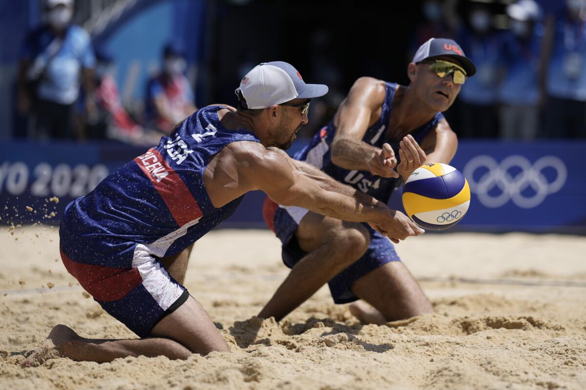 Phil Dalhausser and Nick Lucena are on their knees in the sand while trying to reach the ball.