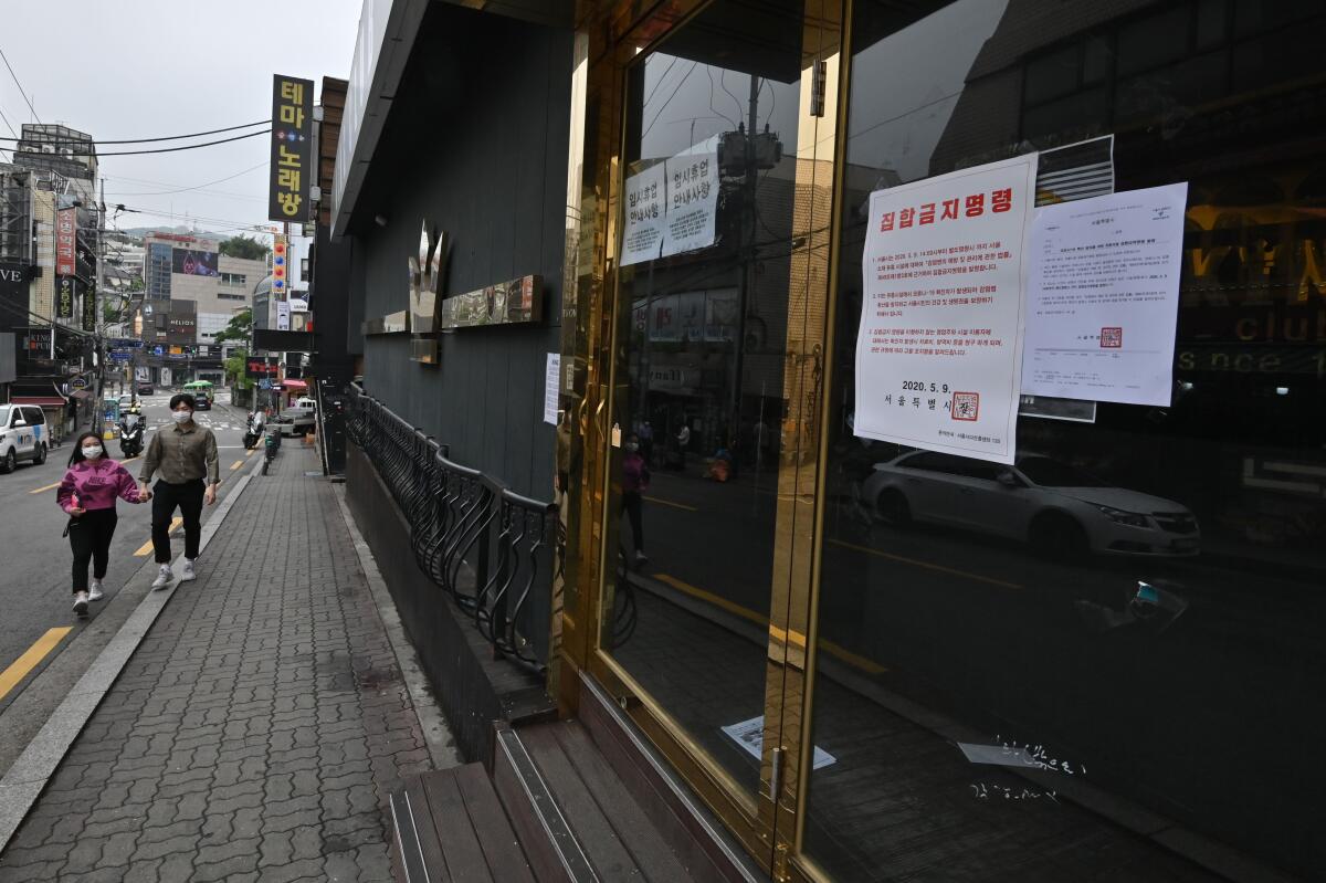 A couple wearing masks walk past a nightclub, now closed after a visit by a confirmed COVID-19 patient, in the popular nightlife district of Itaewon in Seoul on May 10, 2020.