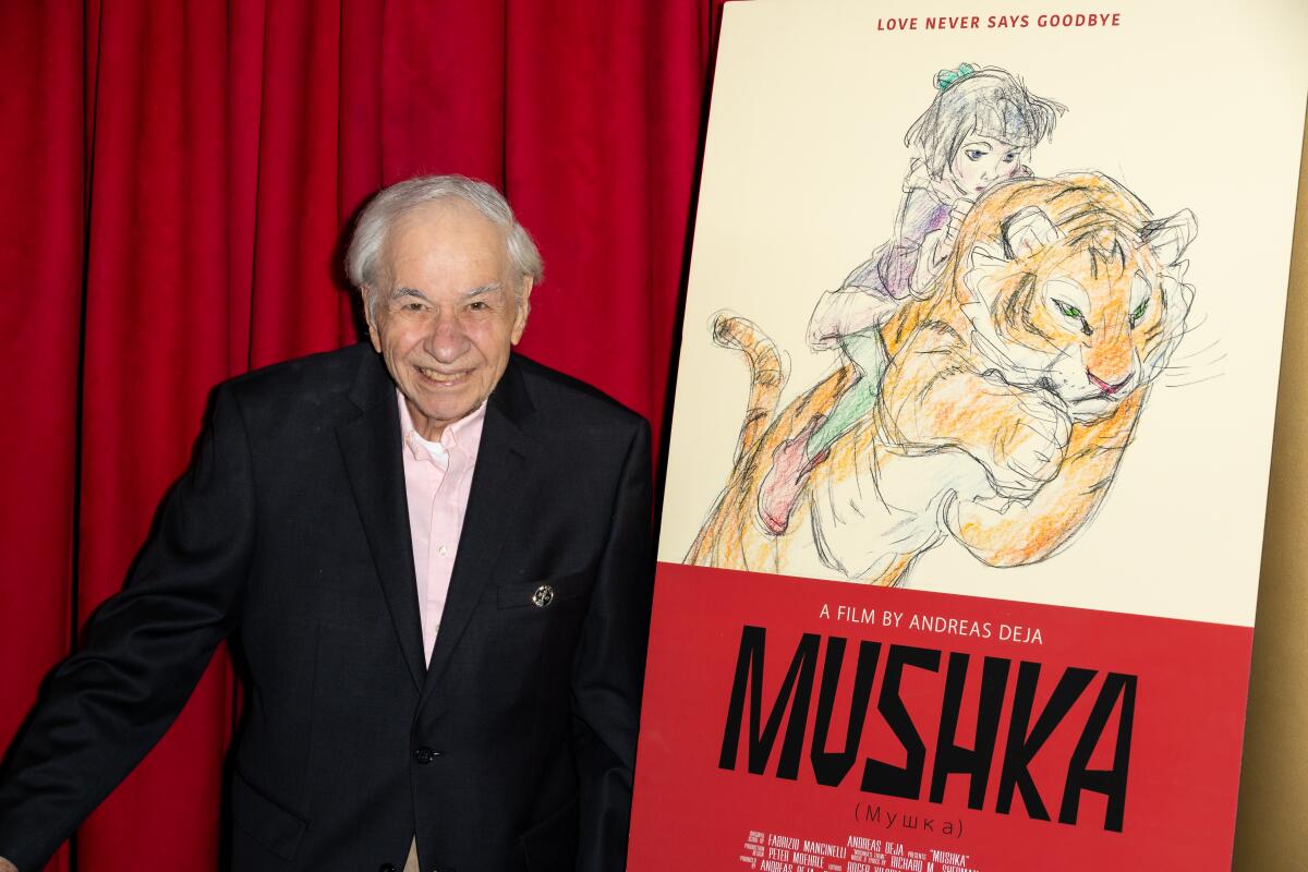Richard M. Sherman stands smiling next to a poster for "Mushka."