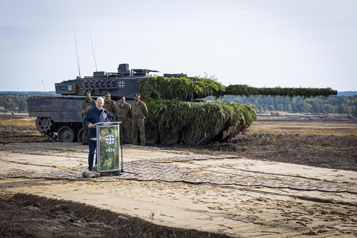 German Chancellor Olaf Scholz speaks to soldiers in front of a tank 