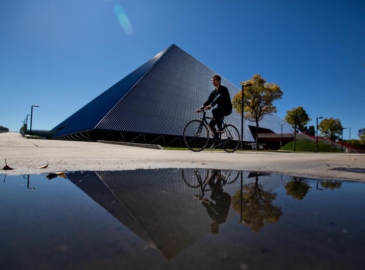 A cyclist is seen in front of a pyramid-shaped structure.