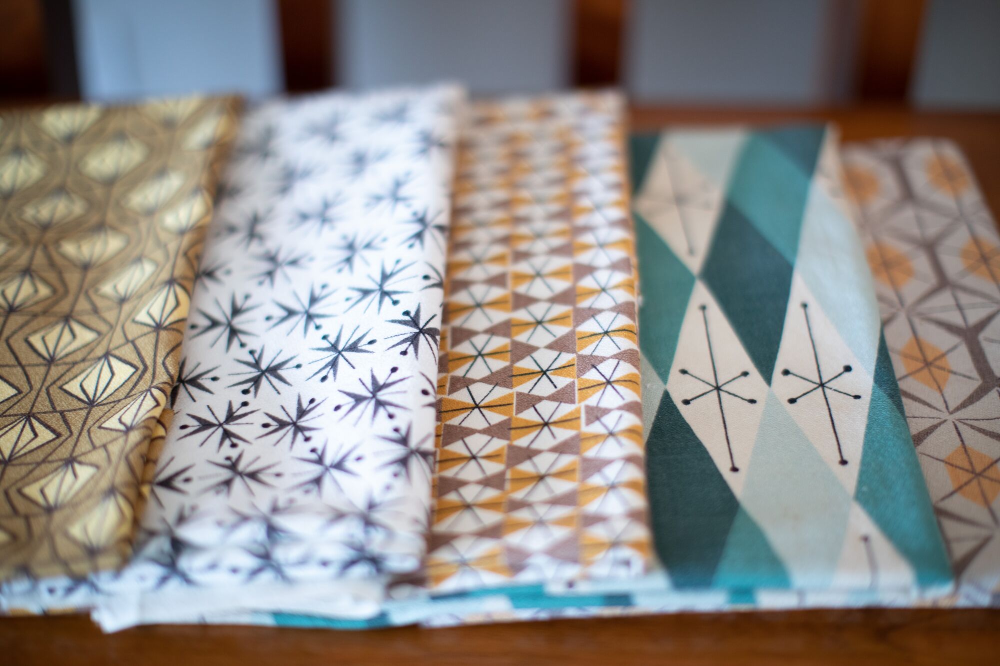 Modernist fabrics covered in geometric patterns are displayed in tidy arrangement on a wooden surface.
