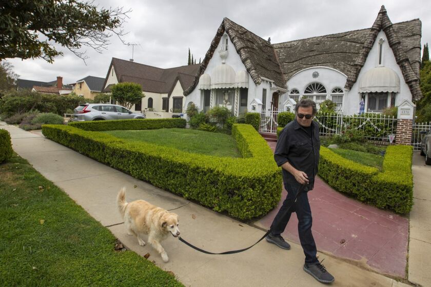 LOS ANGELES, CALIF. -- TUESDAY, MAY 7, 2019: Erich Anderson, who has lived in the Carthay Circle neighborhood since 1997 and is upset about the impact of SB50 on neighborhoods like Carthay, walks his dog, Becky past a historic storybook home in the Los Angeles community Tuesday, May 7, 2019. Residents are upset about the impact of SB50 on neighborhoods like Carthay, where neighbors fear their single-family hood will be destroyed by 8-story apartment buildings. There are lots of Spanish revival, tudor and storybook architecture homes in the neighborhood. All the utility lines are underground with lots of trees and nice walkable streets. (Allen J. Schaben / Los Angeles Times)