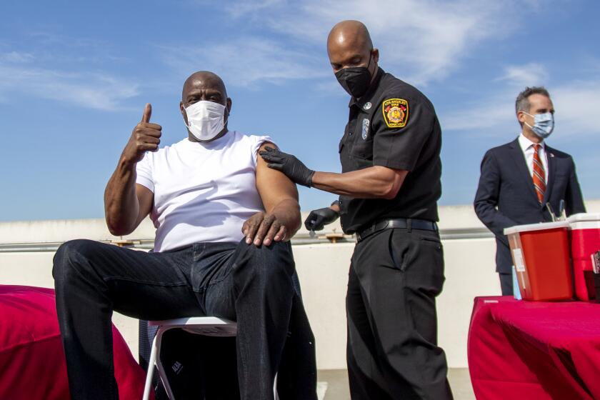 LOS ANGELES, CA - MARCH 24, 2021: Magic Johnson gives a thumbs up after getting a vaccine from Los Angeles Fire Chief Ralph Terrazas on the rooftop of parking structure at USC as a part of a vaccination awareness event at USC on March 24, 2021 in Los Angeles, California. L.A. Mayor Eric Garcetti is in the background. (Gina Ferazzi / Los Angeles Times)