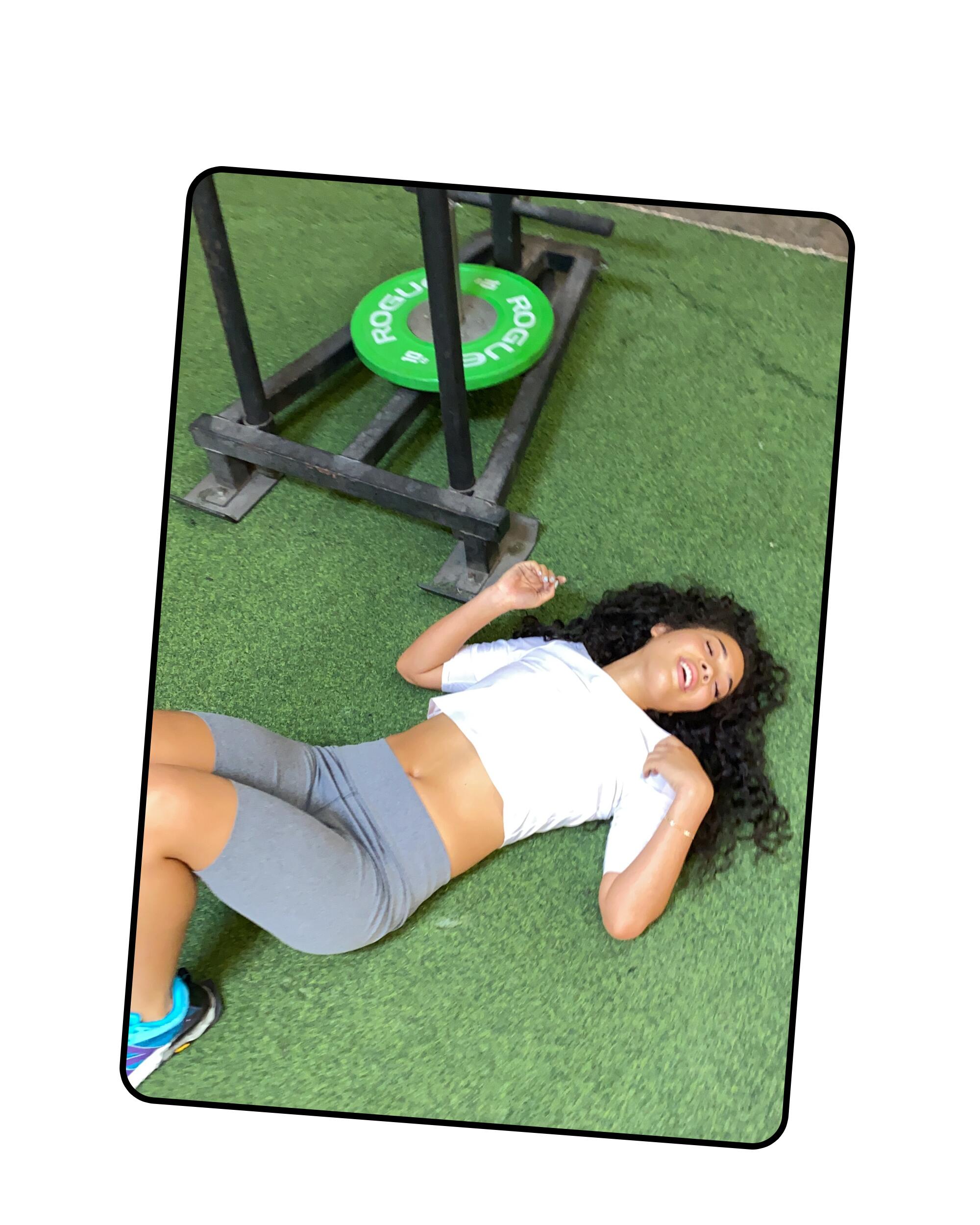 A woman with long curly hair lies down next to gym equipment
