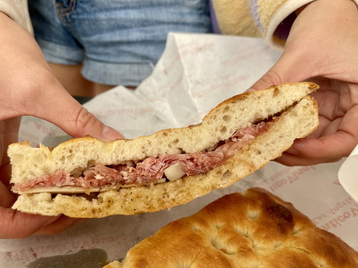 Hands hold a salame, Pecorino and truffle honey sandwich, displaying its meager filling.