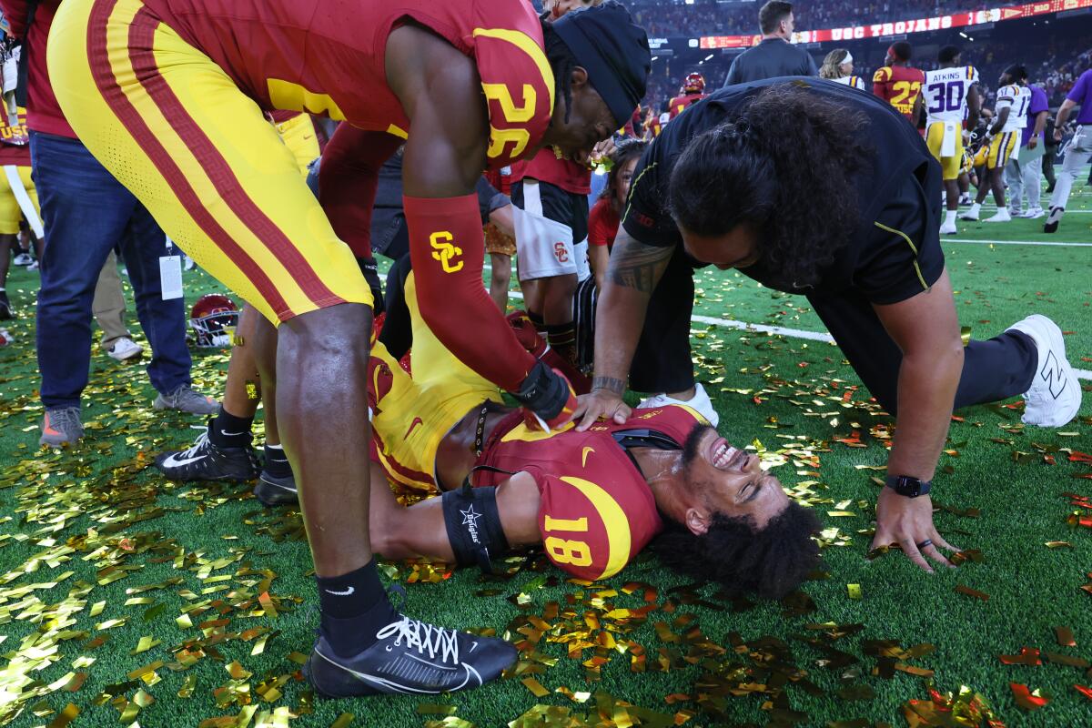 USC linebacker Eric Gentry lies on the field surrounded by confetti as he celebrates with a teammate and coach.