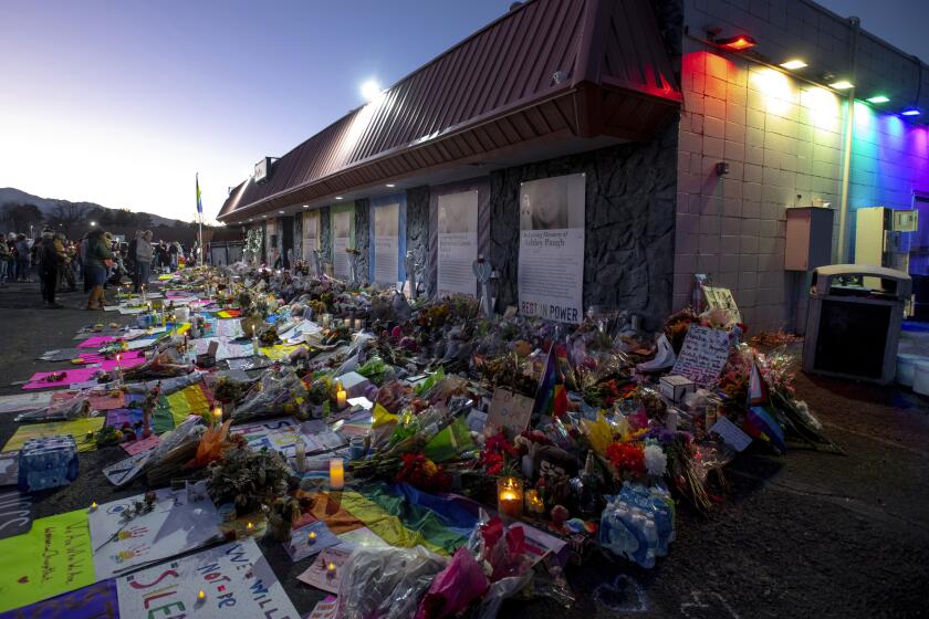 File - Mourners gather outside Club Q to visit a memorial, which has been moved from a sidewalk outside of police tape that was surrounding the club, on Friday, Nov. 25, 2022, in Colorado Spring, Colo. The suspect accused of entering the gay nightclub clad in body armor and opening fire with an AR-15-style rifle, killing five people and wounding 17 others, is set to appear in court again Tuesday, Dec. 6 to learn what charges prosecutors will pursue in the attack, including possible hate crime counts. (Parker Seibold/The Gazette via AP, File)