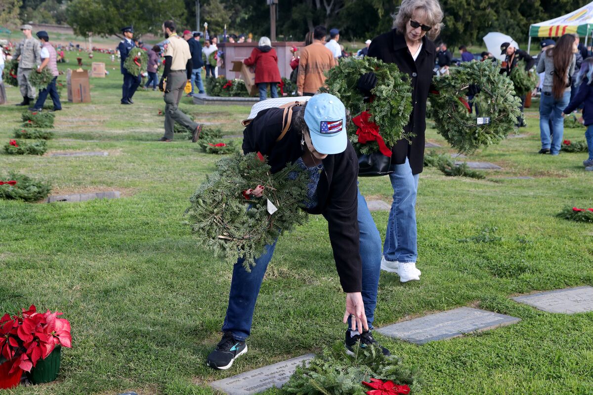 Volunteers place wreaths atop tombstones during National Wreaths Across America Day. 