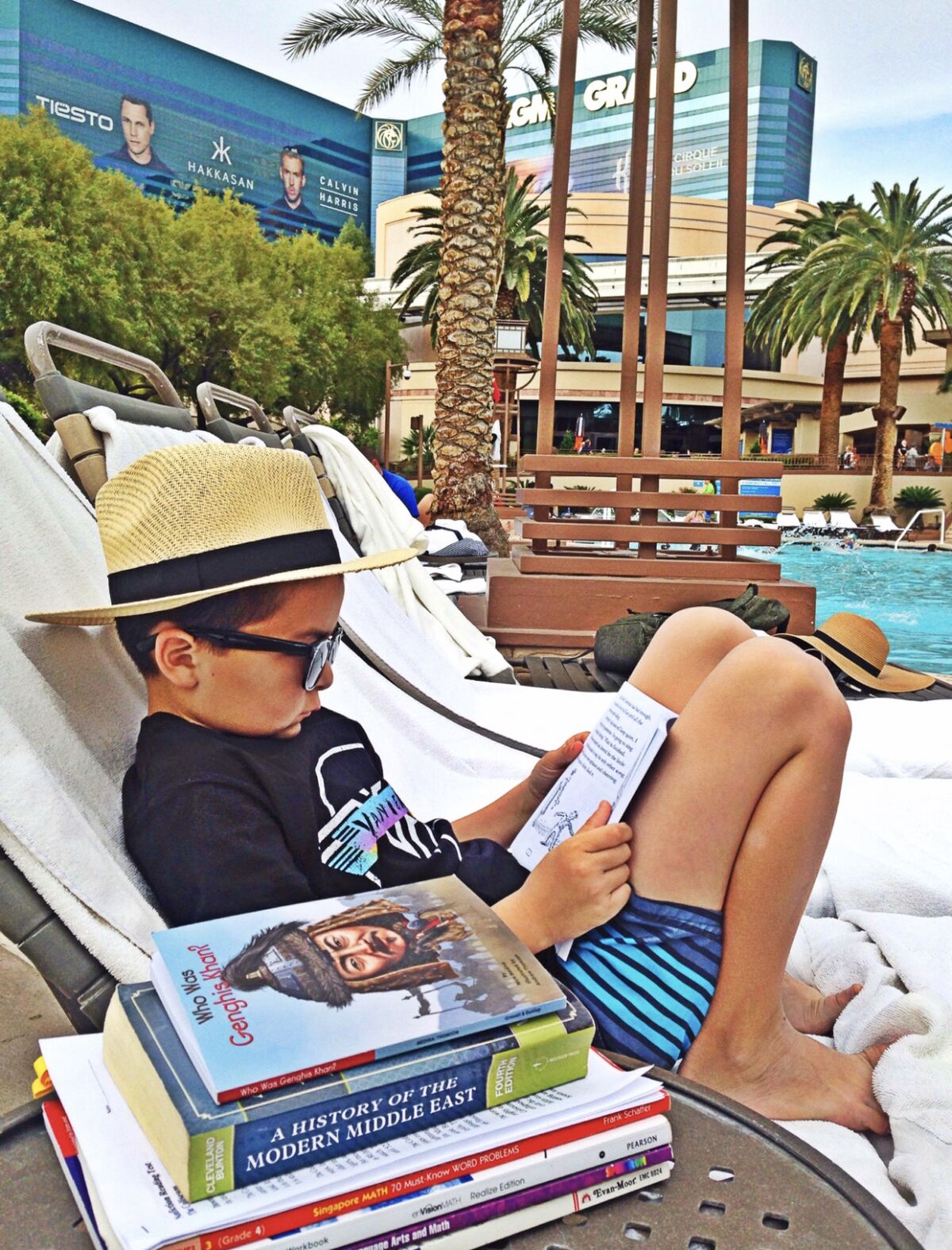 A boy reads a book in a lounge chair by a pool