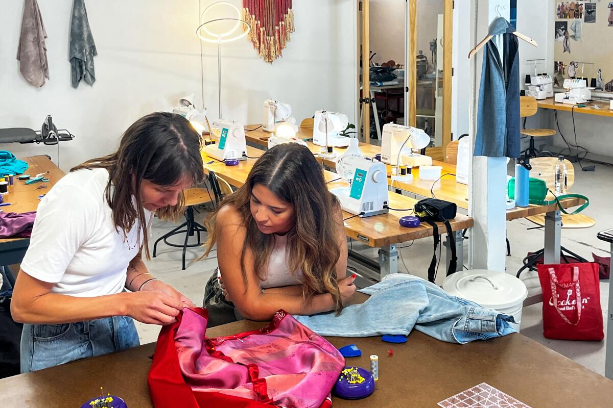 Two women lean over a sewing project in a studio.