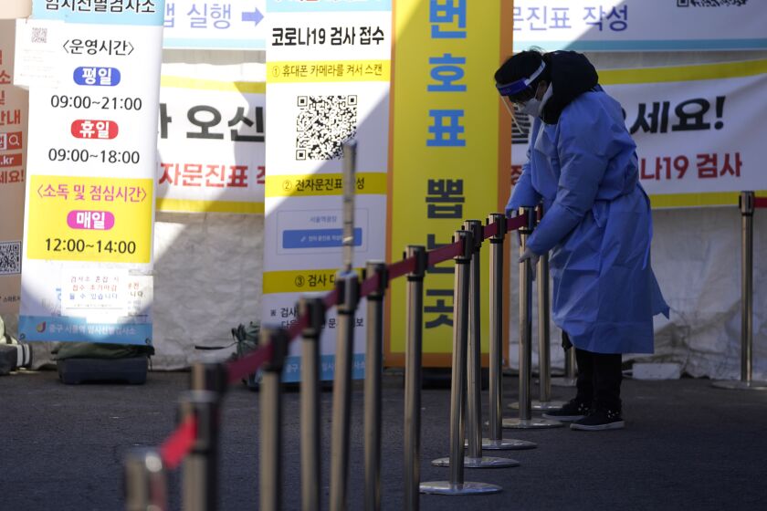 A health worker wearing protective gear prepares for visitors in the sub-zero temperatures at a temporary screening clinic for the coronavirus in Seoul, South Korea, Friday, Jan. 14, 2022. (AP Photo/Lee Jin-man)