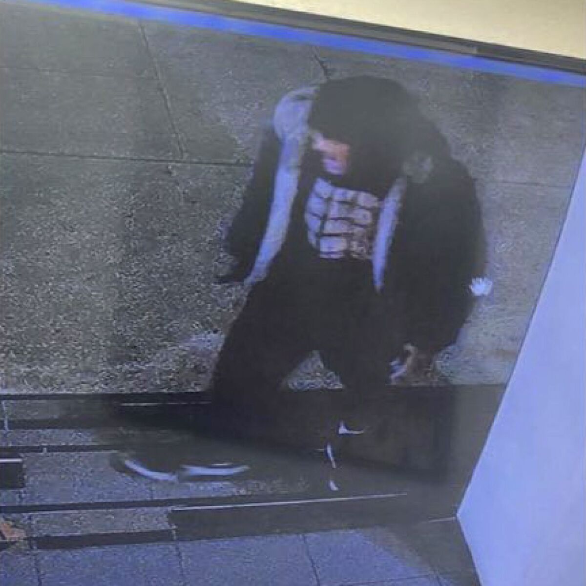 Surveillance image of a man wearing a black cap, black shirt, black shorts, black trousers and black shoes