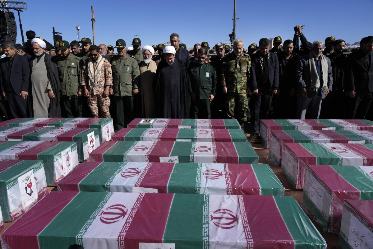 Varias personas rezan junto a los ataúdes, cubiertos con banderas de Irán,