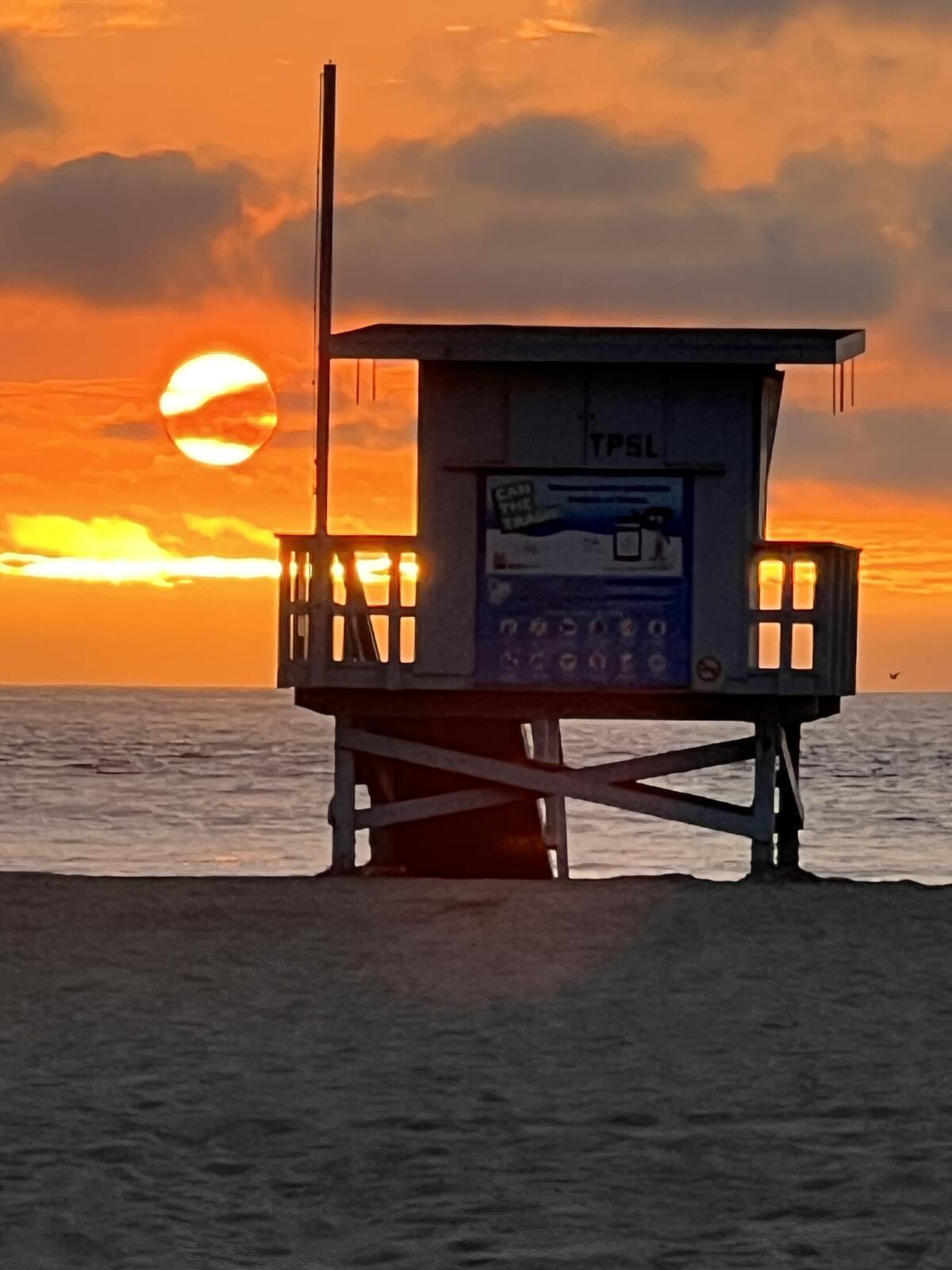 The sun nears the Pacific horizon behind a lifeguard tower on Venice Beach.