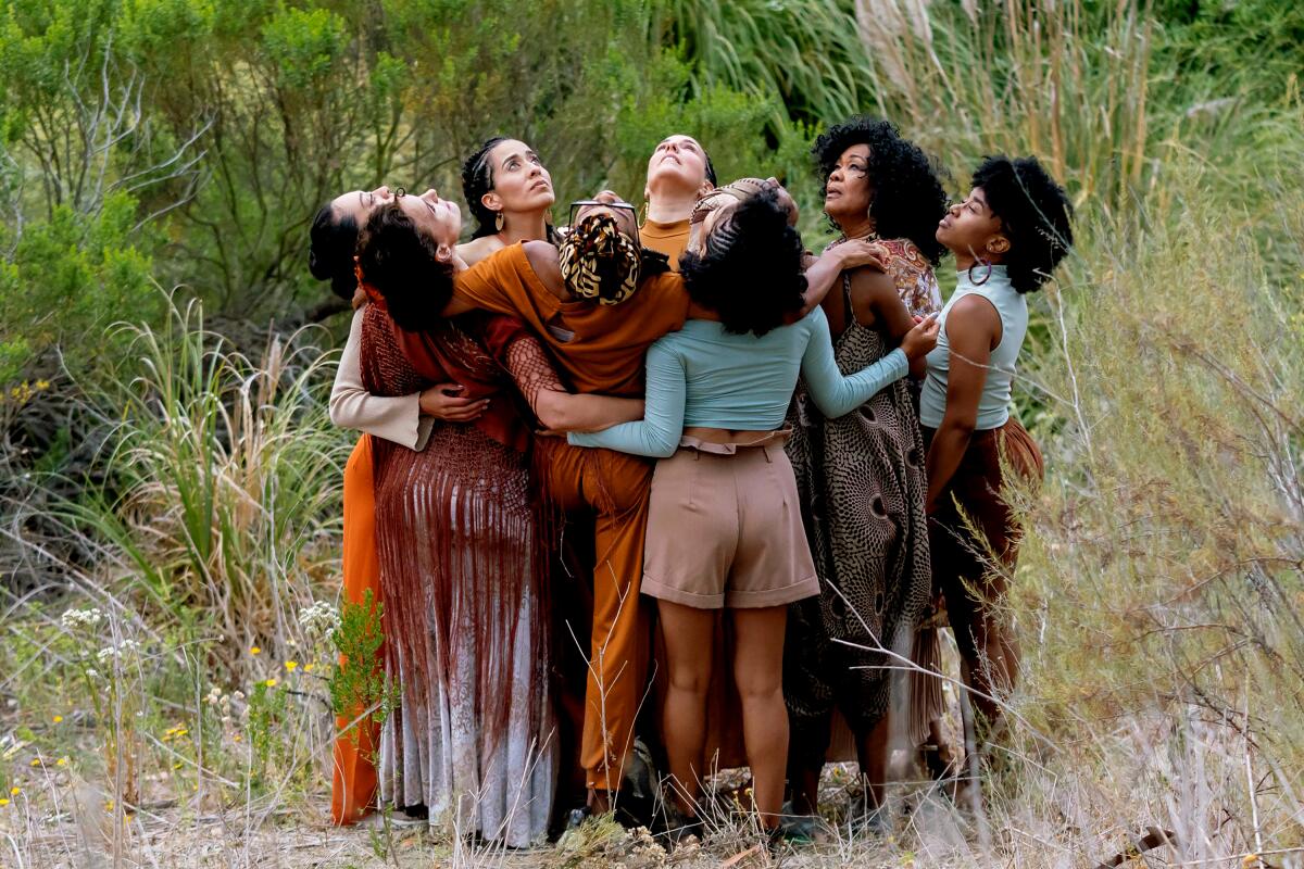 Dancers surrounded by greenery gather in a circle, looking up. 