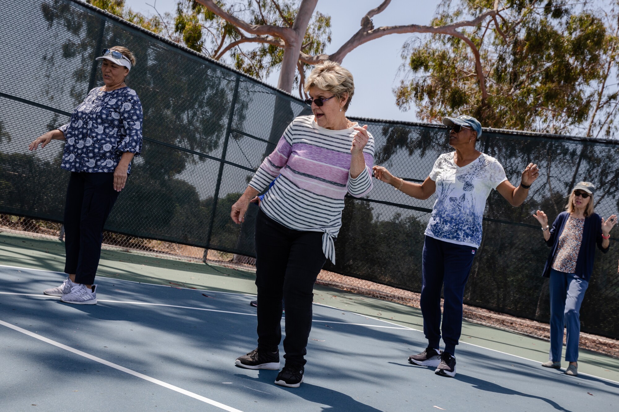 four older adults dance on a tennis court outside