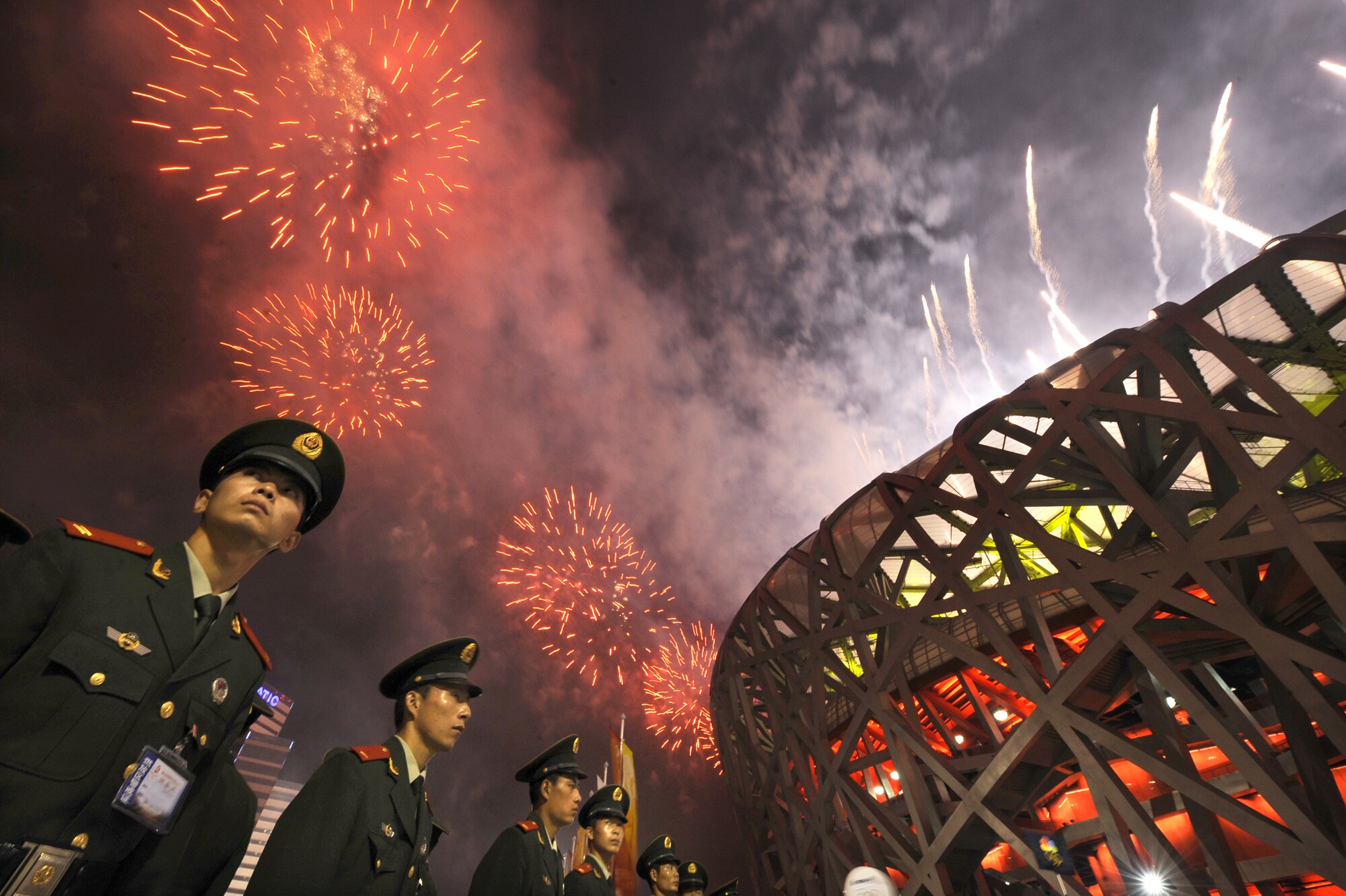 Soldiers stand outside the "bird's nest" stadium as fireworks go off above