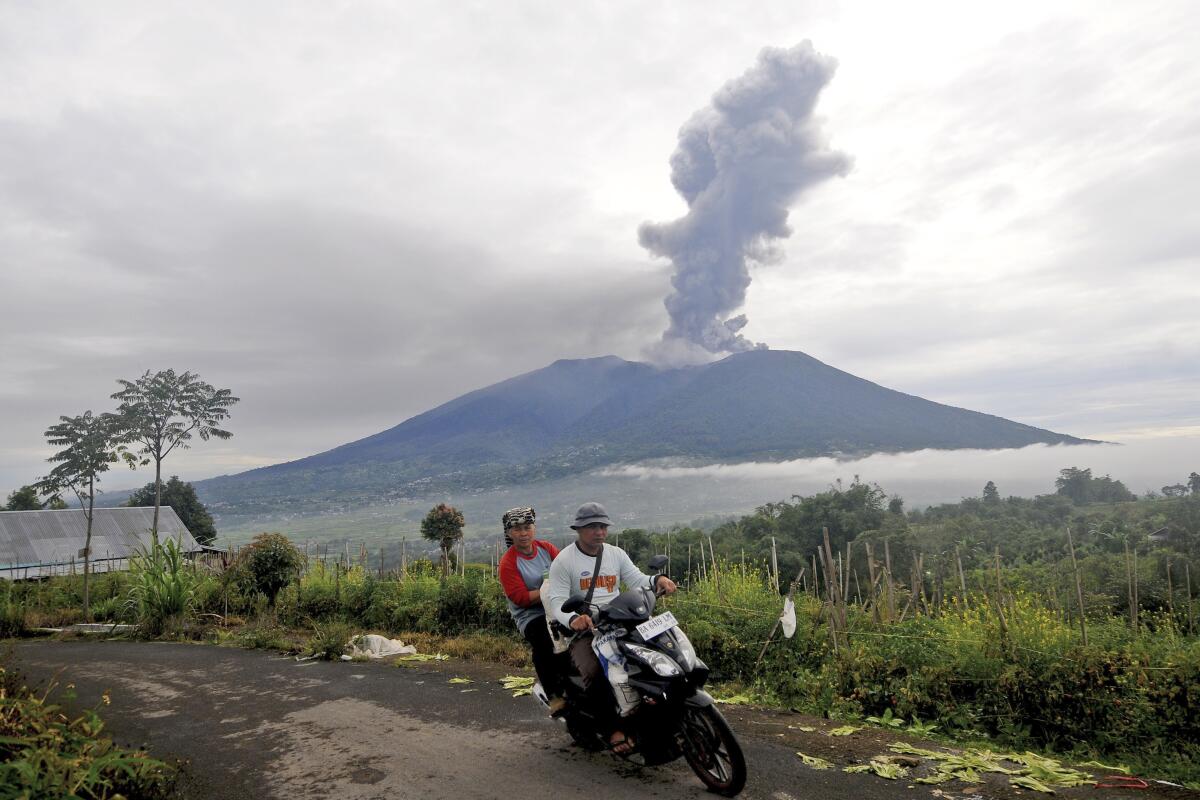 Two people on a motorbike with Mt. Merapi erupting in the background