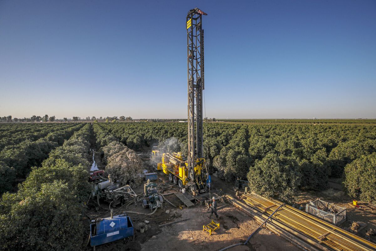 A drilling rig constructs a water well amid a commercial orchard