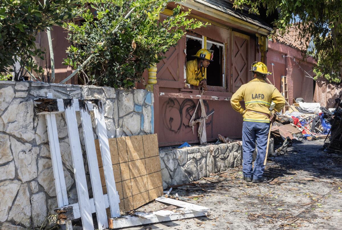 A firefighter leans through an open window toward a colleage outside.