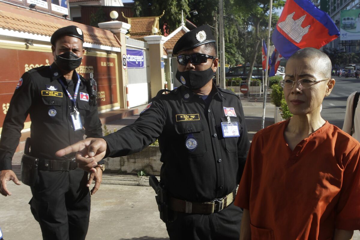 Court securities direct Cambodian-American lawyer Theary Seng, right, dressed in a prison-style orange outfit, to the entrance of Phnom Penh Municipal Court in Phnom Penh, Cambodia, Tuesday, Jan. 4, 2022. Cambodian security forces on Tuesday briefly detained Theary, a prominent rights activist, as she walked barefoot near the prime minister’s residence in Phnom Penh, wearing the orange outfit and Khmer Rouge-era ankle shackles. She was released, shortly afterwards, and arrived at the Phnom Penh court for the resumption of her trial on treason charges. (AP Photo/Heng Sinith)