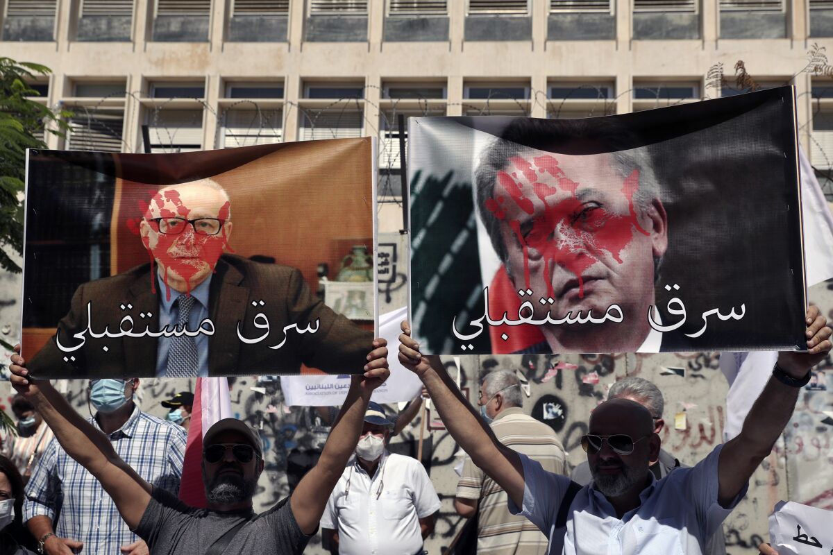 Bank customers hold up defaced posters of Riad Salameh, the governor of Lebanon's Central Bank, right, and Makram Sadir, secretary general of the Association of Banks in Lebanon, with Arabic that reads: "Stole my future," during a protest in front of the Central Bank in Beirut, Lebanon, Wednesday, Oct. 6, 2021. Dozens of Lebanese gathered outside a bank in Beirut's downtown demanding that they be allowed to withdraw their deposits that have been blocked amid Lebanon's severe financial and economic crisis. (AP Photo/Bilal Hussein)