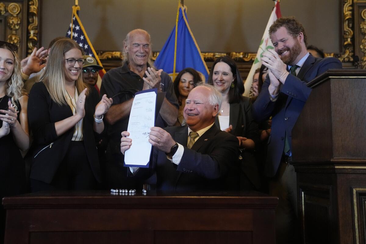 Minnesota Gov. Tim Walz, middle, holds the bill signed to legalize recreational marijuana for people over the age of 21.